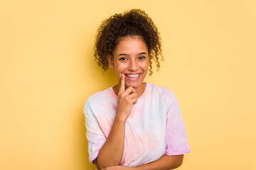 Young Brazilian curly hair cute woman isolated on yellow background smiling happy and confident, touching chin with hand.