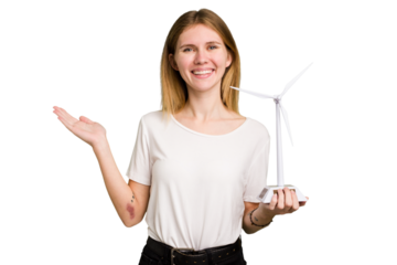 Young caucasian woman holding a small wind energy mill isolated showing a copy space on a palm and holding another hand on waist.