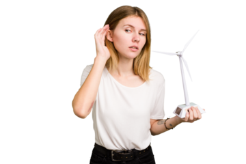 Young caucasian woman holding a small wind energy mill isolated trying to listening a gossip.