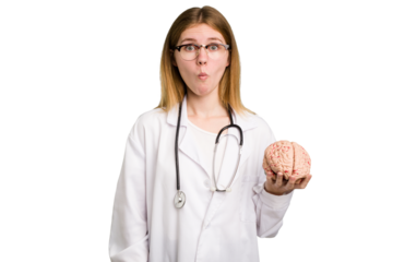 Young doctor caucasian woman holding a brain isolated shrugs shoulders and open eyes confused.