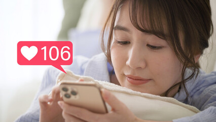 スマートフォンを操作をするパジャマ姿の若い女性