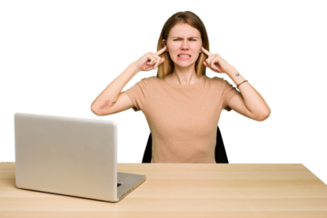 Young caucasian woman in a workplace working with a laptop isolated covering ears with fingers, stressed and desperate by a loudly ambient.