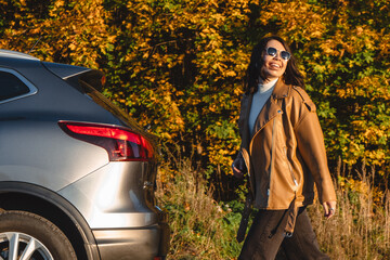 An autumn forest background with a smiling woman walking next to her car
