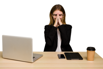 Young business caucasian woman working on her workplace cutout isolated holding hands in pray near mouth, feels confident.