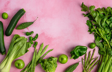 Healthy green vegetables on pink texture arranged horizontally