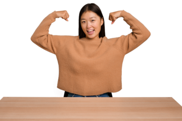 Young asian woman sitting on a table isolated showing strength gesture with arms, symbol of feminine power