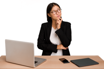 Young business asian woman sitting on a table isolated thinking and looking up, being reflective, contemplating, having a fantasy.