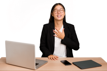 Young business asian woman sitting on a table isolated laughs out loudly keeping hand on chest.