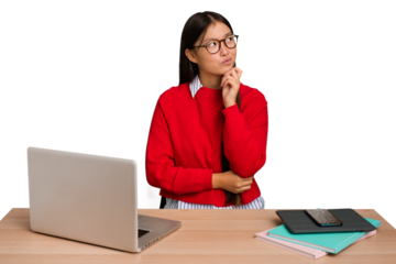 Young student asian woman in a workplace with a laptop isolated looking sideways with doubtful and skeptical expression.