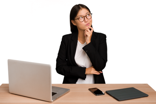 Young business asian woman sitting on a table isolated thinking and looking up, being reflective, contemplating, having a fantasy.