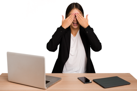 Young business asian woman sitting on a table isolated covers eyes with hands, smiles broadly waiting for a surprise.