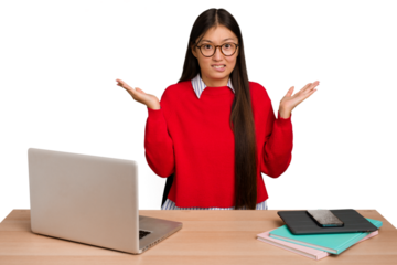 Young student asian woman in a workplace with a laptop isolated confused and doubtful shrugging shoulders to hold a copy space.
