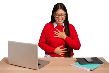 Young student asian woman in a workplace with a laptop isolated laughs happily and has fun keeping hands on stomach.