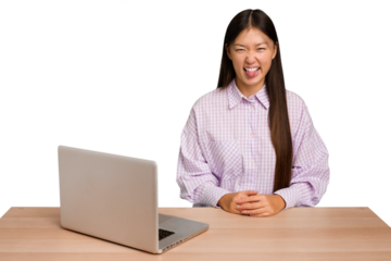 Young student asian woman in a workplace with a laptop isolated funny and friendly sticking out tongue.