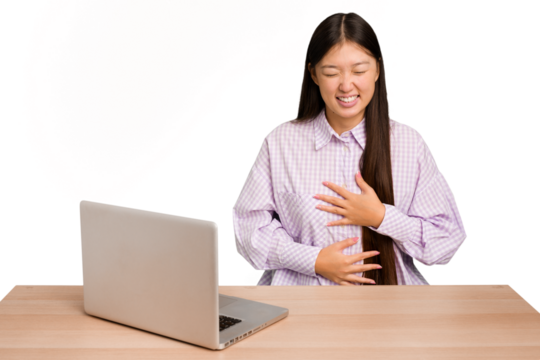 Young student asian woman in a workplace with a laptop isolated laughs happily and has fun keeping hands on stomach.