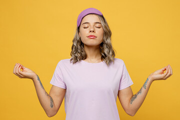 Calm young woman wear purple pyjamas jam sleep eye mask rest relax at home spread hands in yoga om...
