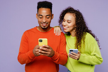 Young couple two friends family man woman of African American ethnicity wear casual clothes together hold in hand use mobile cell phone watch memes together isolated on plain light purple background. - obrazy, fototapety, plakaty