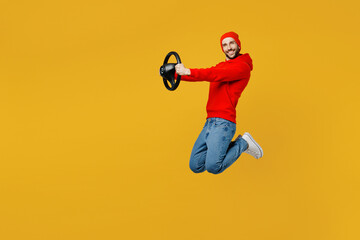 Fototapeta na wymiar Full body side view fun young caucasian man wear red hoody hat look camera jump high hold steering wheel driving car isolated on plain yellow color background studio portrait People lifestyle concept
