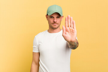 Young caucasian handsome man isolated on yellow background standing with outstretched hand showing stop sign, preventing you.