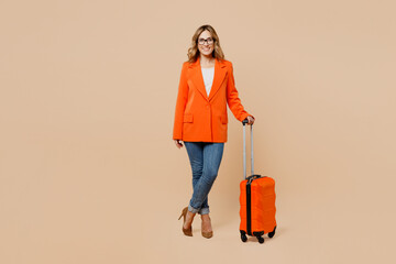 Full body traveler business woman wear formal orange suit glasses hold bag isolated on plain beige background studio. Tourist travel abroad in free time rest getaway. Air flight trip journey concept.