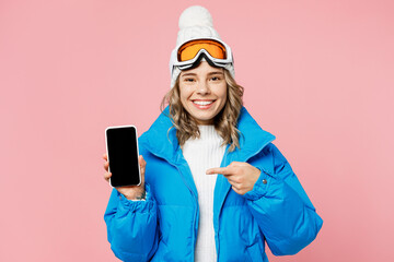 Snowboarder woman in blue suit goggles mask hat ski jacket hold use show mobile cell phone blank screen isolated on plain pastel pink background Winter extreme sport hobby weekend trip relax concept © ViDi Studio