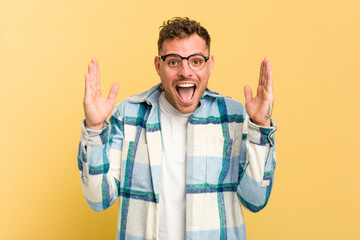Naklejka premium Young caucasian handsome man isolated on yellow background receiving a pleasant surprise, excited and raising hands.