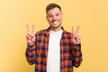 Young caucasian handsome man isolated on yellow background showing victory sign and smiling broadly.