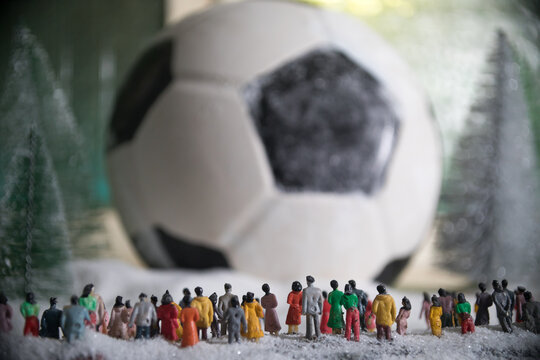 World cup at wintertime concept. Football (Soccer) ball on snowy decorated table with toy miniatures. New Year Christmas theme. Selective focus.