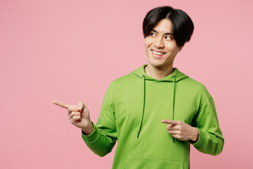 Young fun man of Asian ethnicity wear green hoody point index finger aside indicate on workspace...