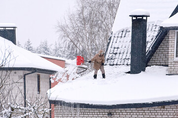 Person removing snow from country house during snowstrom, snow removal. Shoveling snow on roof of...