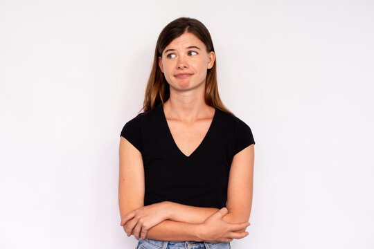 Portrait of young woman looking away with scorn over white background. Caucasian lady wearing black T-shirt and jeans standing with folded arms. Mistrust concept