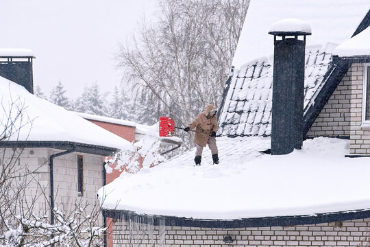 Person Removing Snow From Country House During Snowstrom, Snow Removal. Shoveling Snow On Roof Of Building. Person With Shovel Throwing Snow From Roof. Clean Snowy Rooftop