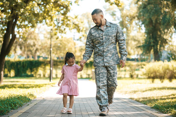 Military man walking with his littile daughter in the park