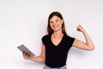 Portrait of happy young woman with touchpad celebrating success. Caucasian lady wearing black T-shirt holding digital tablet and making winning gesture. Success and wireless technology concept