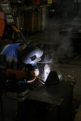 A worker welding metal parts on a construction site. A welder welds parts of a large machine in a...