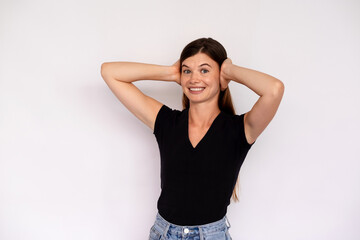 Portrait of happy young woman covering ears with hands over white background. Caucasian lady wearing black T-shirt and jeans undesirable to hear something. Stubbornness concept