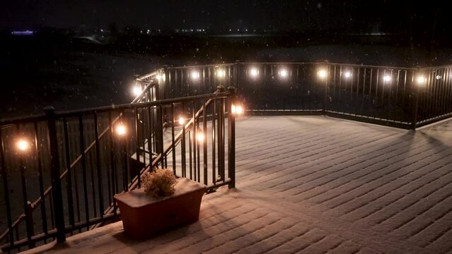 Fresh gently snow falling on a peaceful night - static view of a lit patio or deck