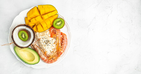 Poke bowl with avocado, shrimp, rice, mango, kiwi and coconut on a light background, healthy and balanced food. Long banner format. top view