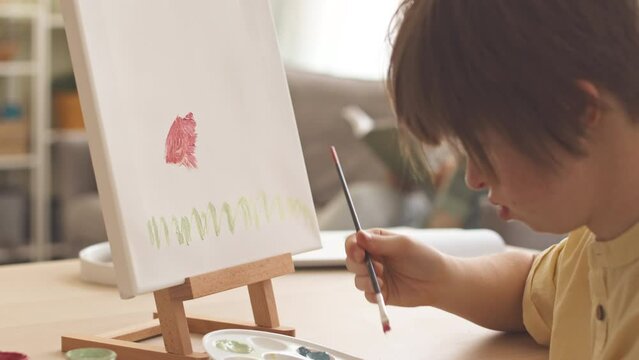 Caucasian teenage girl with down syndrome painting flowers on canvas at home