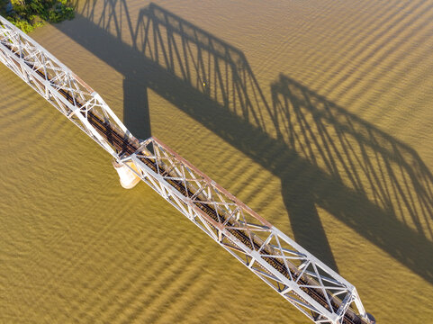 Aerial view of a steel bridge and its shadow over a wide brown river