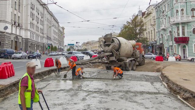 Concrete works and compaction for road construction site with many workers in orange uniform and mixer machine timelapse. Reconstruction of tram tracks