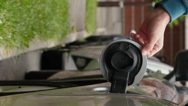 Vertical video of male hand opens the cover of charger and inserts power connector into EV car. Unrecognizable man connects charging cable to electric car and charges the batteries