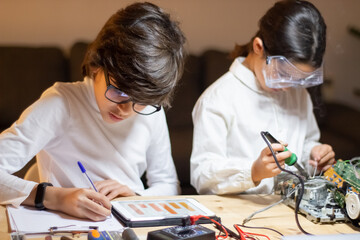 Concentrated children doing experiment in physics together. Girl using solder to create new device....