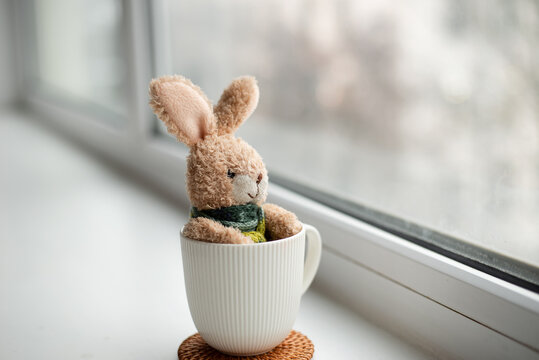 A lonely rabbit in a scarf, sitting alone and looking out the window, A sad stuffed rabbit, the concept of loneliness, International Day of Missing Children. The toy is sick