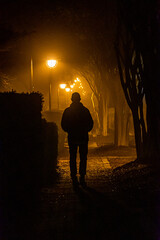 Solomons Island, Maryland, USA A man walks alone in silhouette on a narrow brick sidewalk at night...
