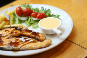 European food, salmon steak with french fries, vegetables and vinegar dressing on a table plate.