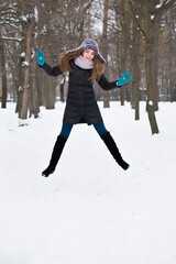 The girl happily jumps on the snow in the winter park