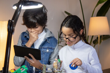 Serious school children creating new project on electronics. Cute girl soldering circuit board while boy thinking over results of experiment. Education, hobby concept - obrazy, fototapety, plakaty
