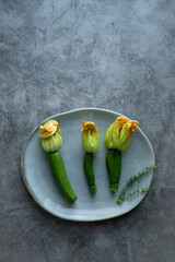 Three zucchini flowers on plate on stone background.
