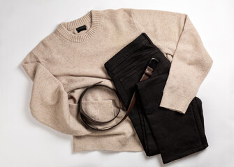 Men's wool beige sweater, black jeans and leather belt. Set of comfortable casual winter or autumn clothes on a light background, flat lay.